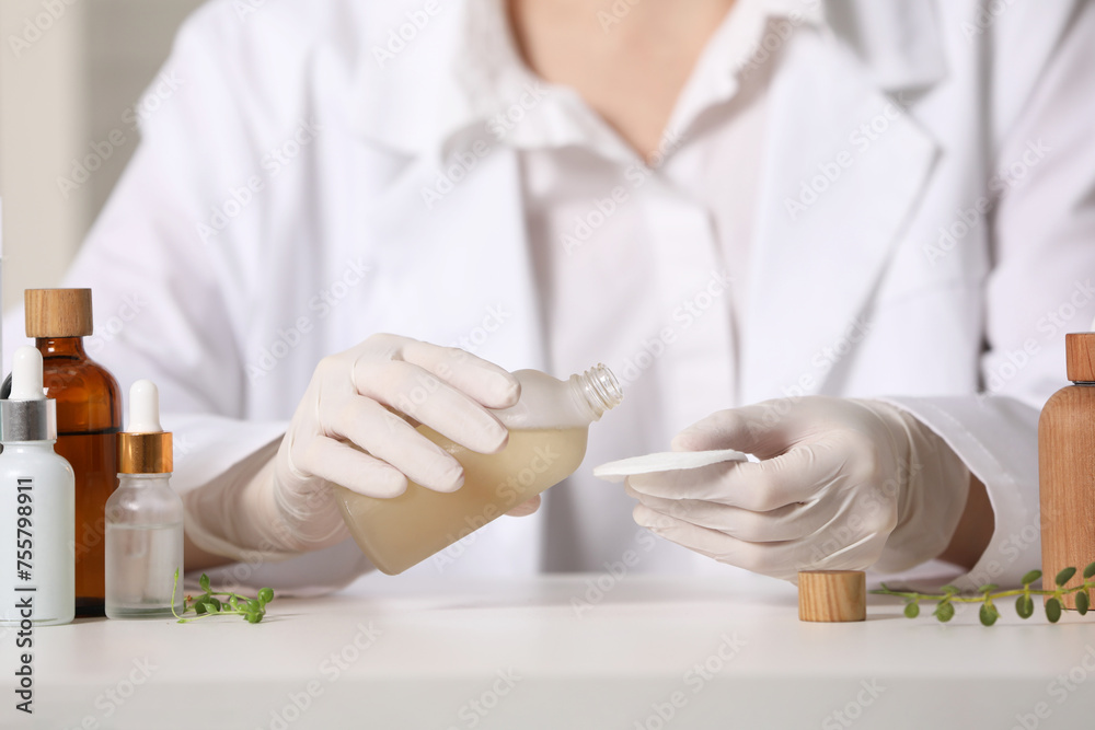 Dermatologist with bottle testing cosmetic product at white table indoors, selective focus Dermatologist with bottle testing cosmetic product at white table indoors, selective focus