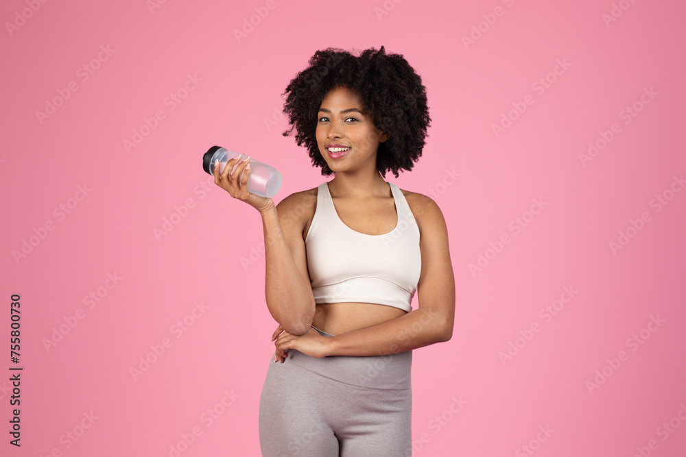Obraz na plátně Smiling black woman with water bottle, sportswear, pink background