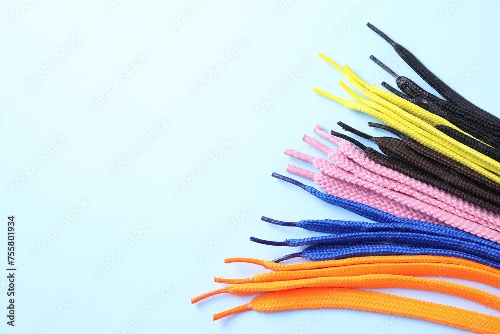 Many colorful shoe laces on light blue background, flat lay. Space for text
