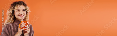 happy woman with curly hair and cup of morning coffee looking away on orange  horizontal banner