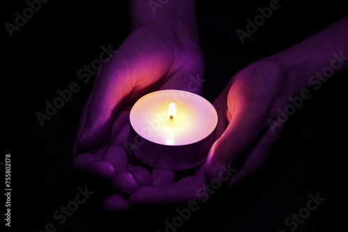 Woman holding burning violet candle in hands on black background, closeup. Funeral attributes