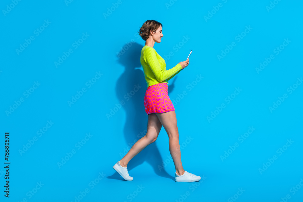 Full length body photo of young lady glamour outfit strolling holding mobile phone satisfied isolated on aquamarine color background