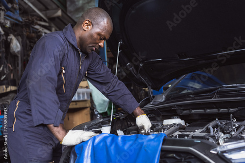 Black car mechanic man working in auto repair garage doing car maintenance and fixing work