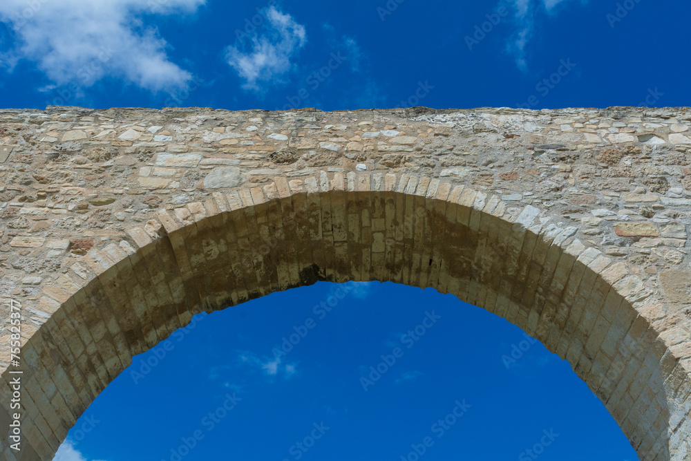 low-angle view of an ancient aqueduct against a blue sky