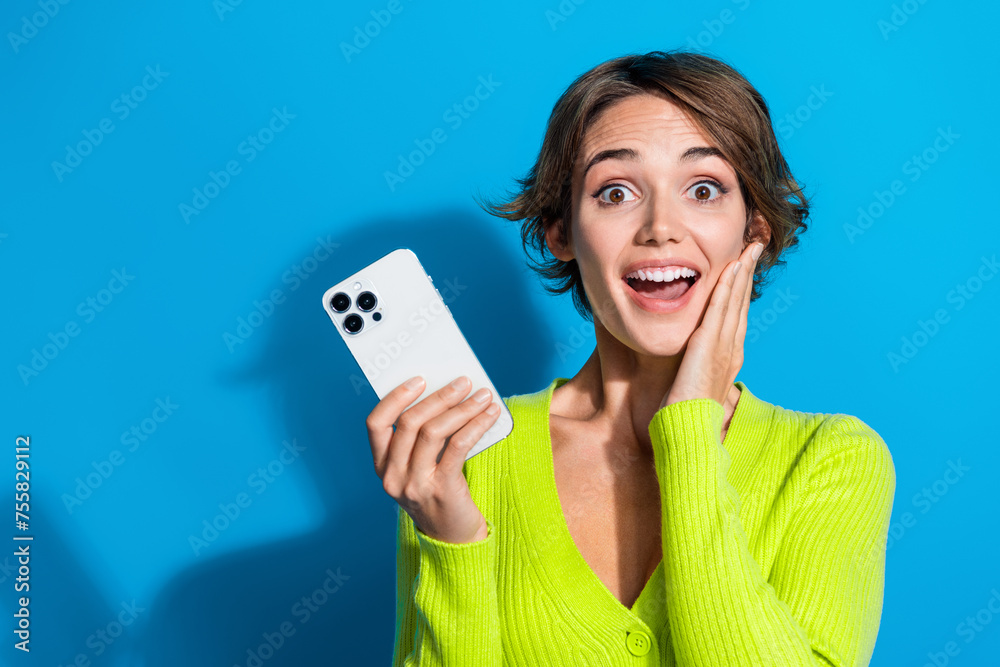 Portrait of young girl touch cheek amazed holding big three camera smartphone original device isolated on aquamarine color background Portrait of young girl touch cheek amazed holding big three camera smartphone original device isolated on aquamarine color background