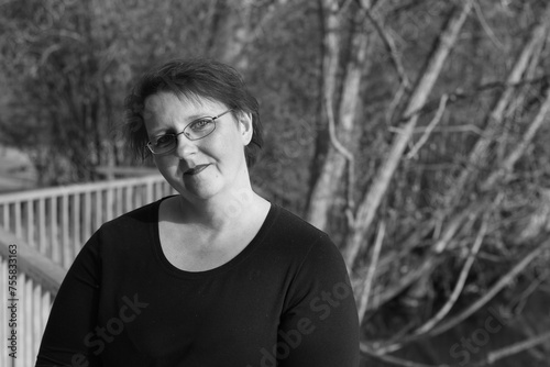 A woman wearing glasses and a black shirt is standing in front of a tree
