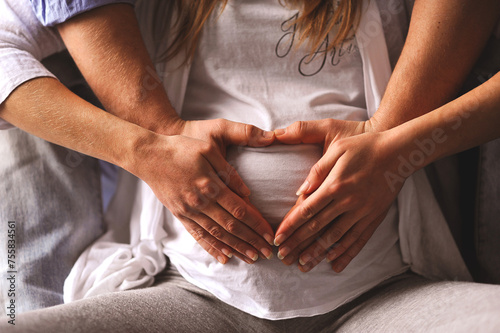 Close up photo of pregnant woman in white t-shirt and her husband make heart shape with hands on pregnant belly. Love concept. Horizontal shot photo