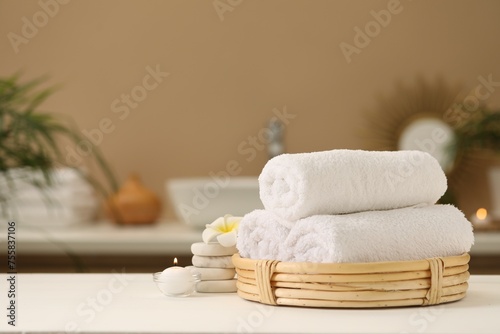 Spa composition. Rolled towels  massage stones  burning candle and plumeria flower on table. Space for text