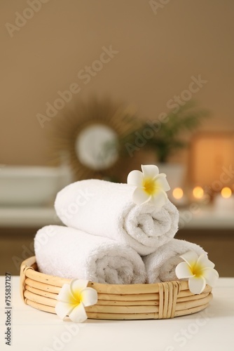 Spa composition. Rolled towels and plumeria flowers on white table indoors. Space for text