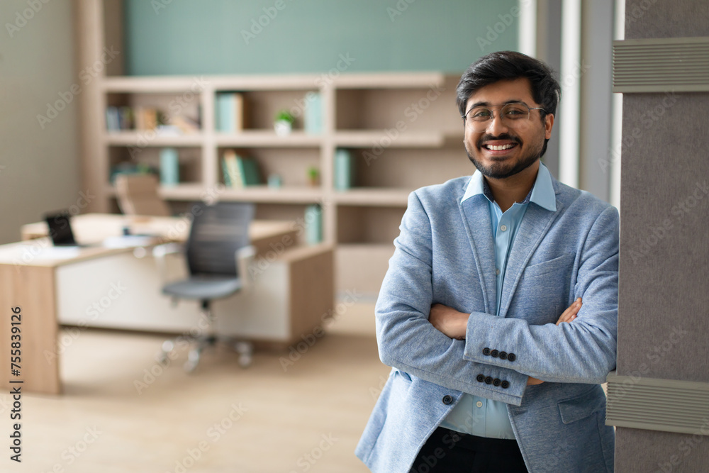 Confident successful Indian businessman stands crossing hands in modern office