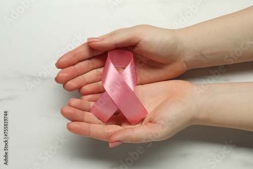 Woman with pink ribbon at white marble table, top view. Breast cancer awareness