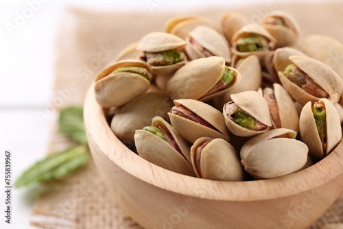 Tasty pistachios in bowl on white table, closeup