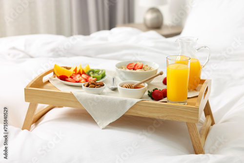 Tasty breakfast served in bed. Oatmeal, juice, fruits, almonds and honey on wooden tray