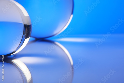 Transparent glass balls on mirror surface against blue background, closeup © New Africa