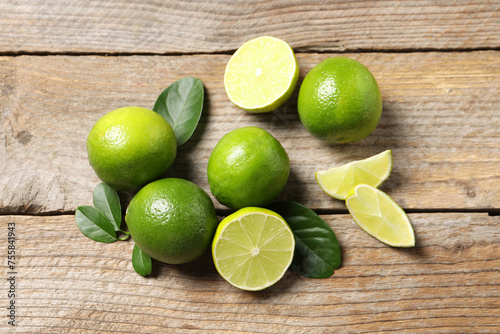 Fresh limes and green leaves on wooden table, flat lay