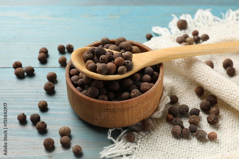 Aromatic allspice pepper grains in bowl and spoon on light blue wooden table Aromatic allspice pepper grains in bowl and spoon on light blue wooden table