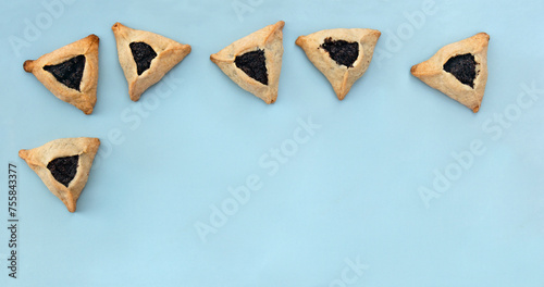 Triangular cookies with poppy seeds ( hamantasch or aman ears ) for jewish holiday of purim celebration on blue background with space for text. Top view, flat lay photo