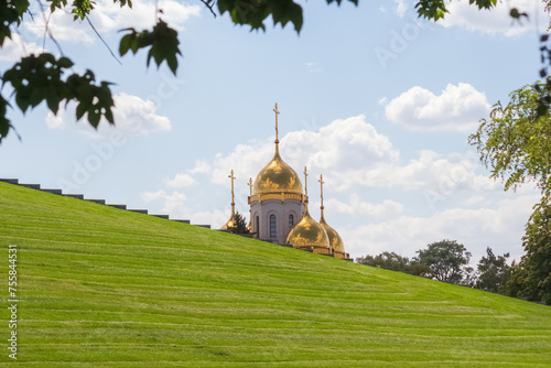 Close-up view of golden cupolas of Russian Orthodox Church of All Saints over green grass on hill in a sunny summer day in Volgograd city, Russia. Russian culture and religion theme.