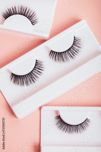 Different fake eyelashes in boxes on trendy pastel pink background. Makeup accessories and beauty cosmetics products for women. Top view, flat lay.