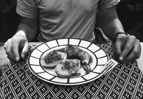 Man preparing to eat his meal at traditional French Basque country restaurant. Chicken leg, baked potato with ratatouille aesthetically served. Black white historic photo.