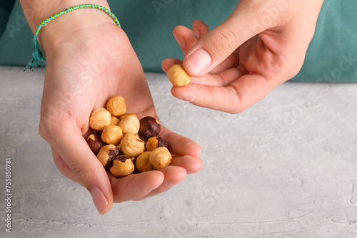 Woman holding peeled whole hazelnuts in her hands at gray table, closeup. Handful of dried hazelnuts in female hands. Healthy snack and healthy eating, Organic vegan fat and protein, food lifestyle