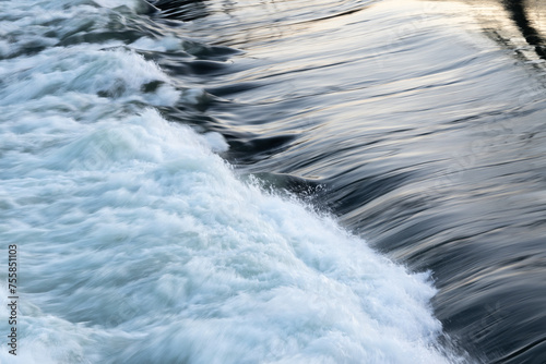 Rapid water flow over barrier, river overflow over dam close up with splash and foam, abstract landscape pastel blue
