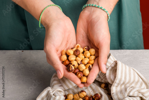 Woman holding peeled whole hazelnuts in her hands at gray table, closeup. Handful of dried hazelnuts in female hands. Healthy snack and healthy eating, Organic vegan fat and protein, food lifestyle