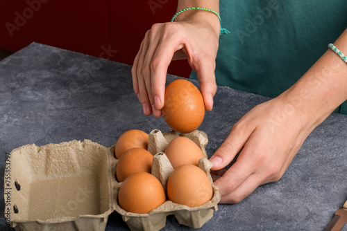 A woman's hand holding an egg taked from the egg box that is on the gray kitchen table, close up, food lifestyle, ready to cooking, cooking blog