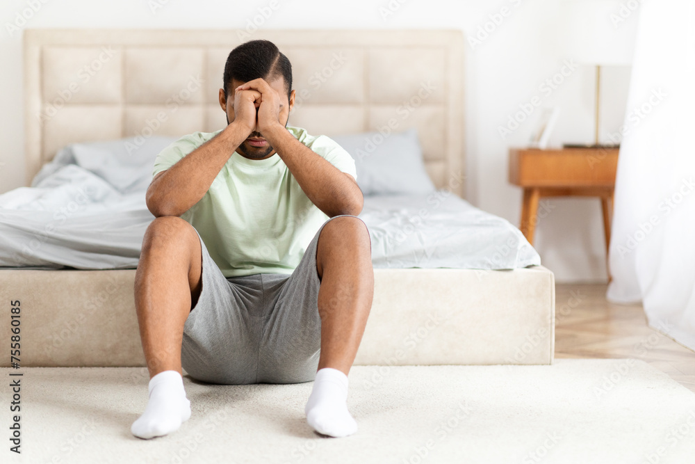 Upset black man sitting on floor at bedroom, crying Upset black man sitting on floor at bedroom, crying