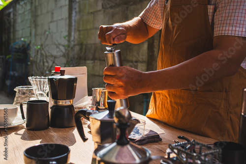 people is grinding coffee beans with manual stainless steel grinder to make black coffee machine, brewing equipment or coffee drip set Dripper on a wooden table In the kitchen at home in the morning