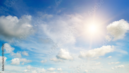 There are white cumulus clouds and a bright sun in the blue sky.
