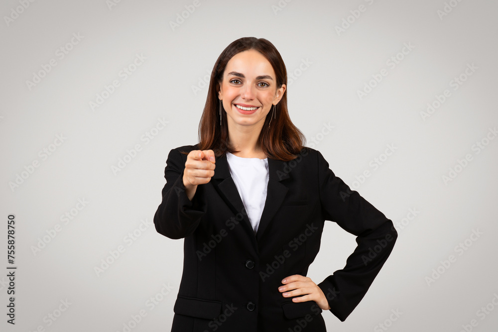 Professional, confident young woman in business attire pointing directly at camera with a friendly smile Professional, confident young woman in business attire pointing directly at camera with a friendly smile