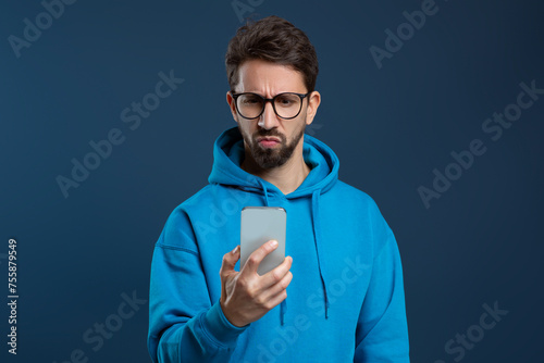 Skeptical man wearing glasses looking at smartphone screen