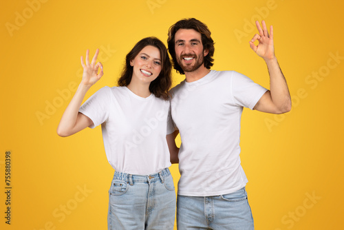 Fényképezés Joyful man and woman in white t-shirts and jeans making the OK hand gesture