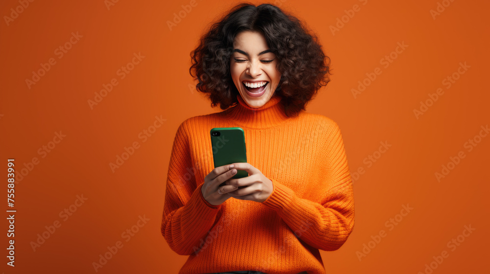 Happy smiling young woman is using her smartphone against orange background