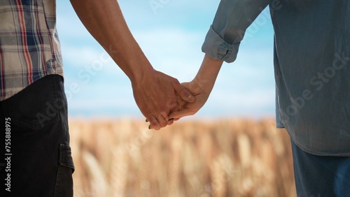 Farmers against large field of wheat and blue sky. Man and woman agronomists workers standing in the farm field, holding hands.