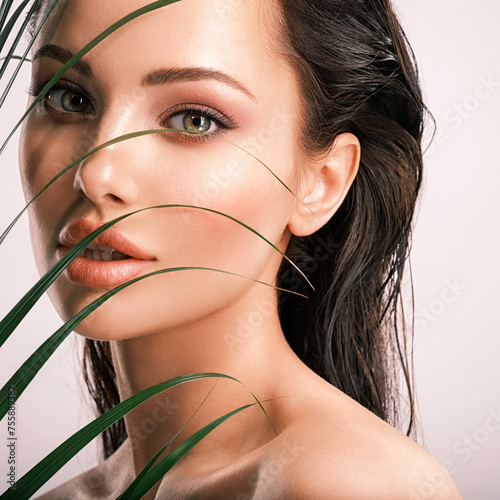 Young beautiful woman with green leaves near face.  White model with clean, health skin of face.