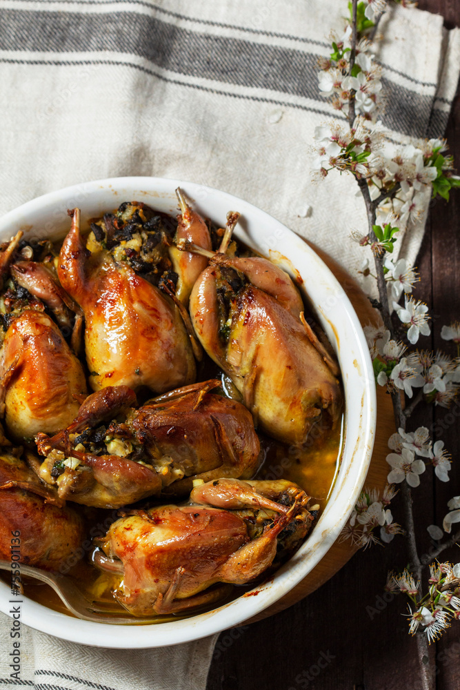 Baked quail stuffed with mushrooms, eggs and bread in a ceramic form on a wooden table.