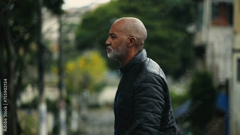 Serious Thoughtful Senior African Descent Man Strolling in City during drizzle rain. One black mature man with concerned expression daydreaming while daily walk