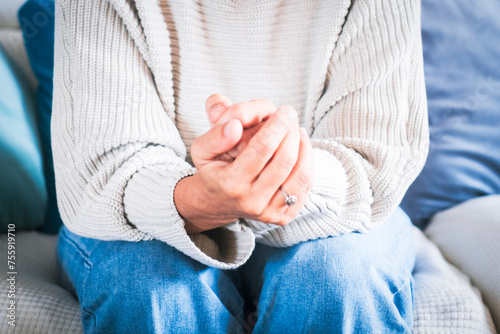 Front view of depressed sad mature woman at home sitting alone on the sofa with hands clasped and looking down. Thoughtful female people and loneliness. Relationship end break out depression health