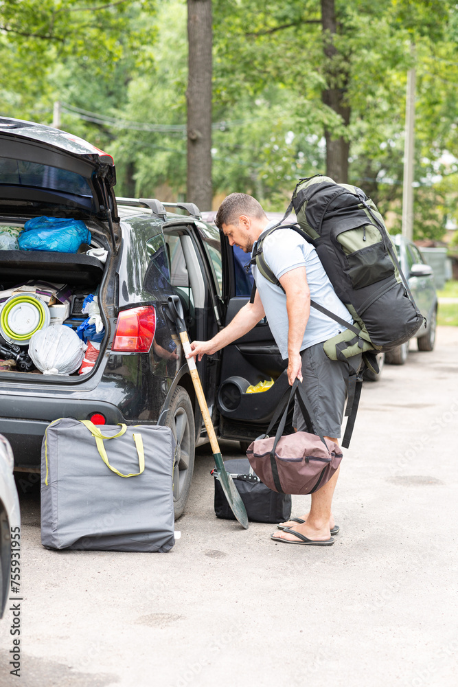 A man loads camping equipment into the trunk of a car