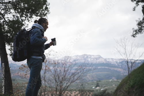 Backpacked male traveler drinking coffee while hiking in mountains. People. Travel. Active tourism and trekking concept