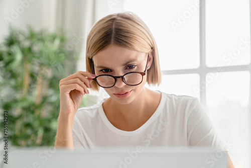 Young caucasian woman wearing glasses watching movies films webinars on laptop. Pensive female freelancer working on problem online, solving issue