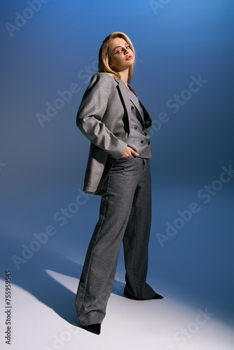 good looking woman with blonde hair in chic silver suit looking at camera on dark blue background