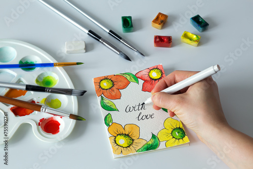 Watercolor painting with an artist's hand, bright painting of flowers. Handmade watercolor card on Valentine's or mother's day, top view.