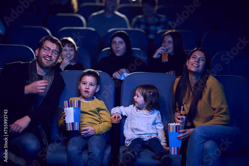A modern family enjoys quality time together at the cinema, indulging in popcorn while watching a movie with their children © .shock
