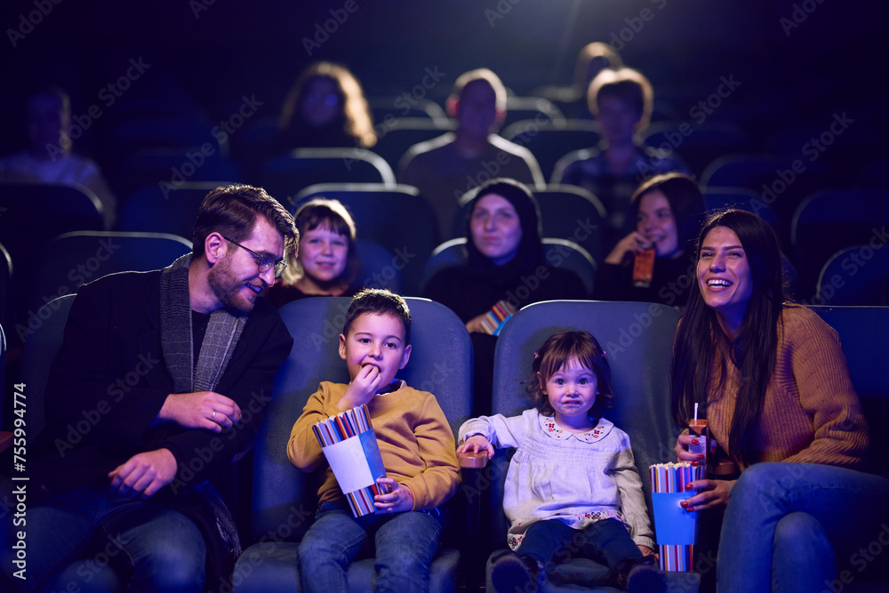 A modern family enjoys quality time together at the cinema, indulging in popcorn while watching a movie with their children