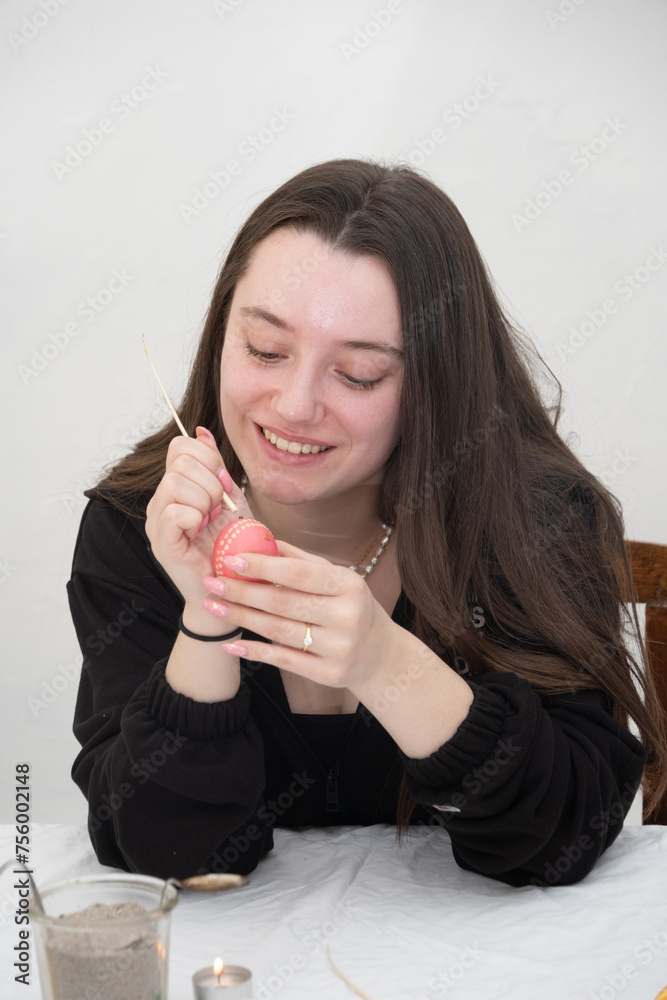 happy smiling young beautiful sexy german female woman with dark brunette hair paints a red Easter egg in Sorbian tradition with a needle head and melted wax. happy smiling young beautiful sexy german female woman with dark brunette hair paints a red Easter egg in Sorbian tradition with a needle head and melted wax.