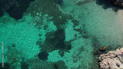 An overhead shot rotating 360 degrees over very transparent Mediterranean Sea waters of a cove with a beach on the island of Mallorca, seeing a varied background of sand and algae. Cove, beach, rocks 