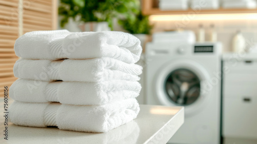 A stack of folded clean white towels on the table against the background of washing machines, laundry room with copy space